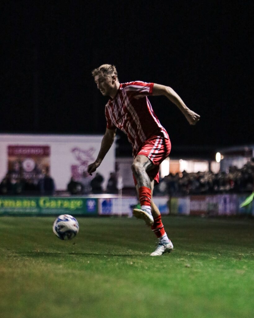 A Bridgwater United player strikes the ball under the floodlights at Fairfax Park